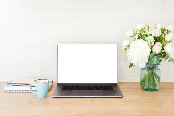 Mesa de escritório com computador portátil com tela em branco mockup, suprimentos, xícara de café, buquê de flores na superfície de madeira. Conceito de espaço de trabalho de mulher de negócios — Fotografia de Stock