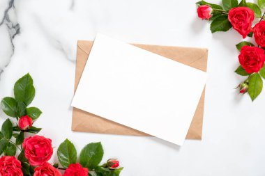 Mermer arka plan üzerinde gül çiçekleri çerçeve ve zanaat kağıt zarf ile boş kartpostal. Sevgililer Günü, Anneler veya Kadınlar Günü için tebrik kartı mockup. Düz döşeme stili kompozisyon, üst görünüm, genel merkez