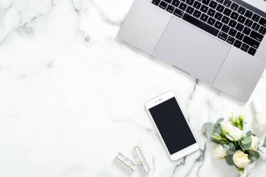 Düz yatıyordu ev ofis masası. Dizüstü bilgisayar, boş ekran akıllı telefon, çiçek buketi, kozmetik ile Kadın çalışma alanı. Üst görünüm kadınsı arka plan. Moda blogger çalışma alanı kavramı.