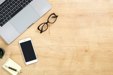 Dizüstü bilgisayar, siyah ekranlı akıllı telefon, kağıt not defteri, kalem, sulu bitki ile modern ahşap ofis masası masa. Kopya alanı ile üst görünüm, düz yatıyordu. Kadınsı çalışma alanı kavramı.