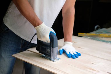 Marangoz marangozluk atölyesinde jig testere makinesi ile bir kontrplak levha biçiyor. Yan görünüm.