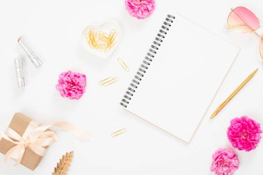 Düz yatıyordu ev ofis masası. Üst görünüm boş kağıt not defteri, pembe gül çiçek tomurcukları, yaprakları, kadın aksesuarları, beyaz arka plan üzerinde hediye kutusu. Kadın masası, moda blogger, güzellik konsepti.