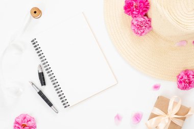Düz yatıyordu ev ofis masası. Boş kağıt not defteri, hasır şapka, pembe gül çiçekleri, şık aksesuarlar ile kadın çalışma alanı. Üst görünüm kadınsı arka plan. Kadın masa, moda blogger, güzellik kavramı