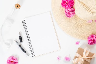 Düz yatıyordu ev ofis masası. Boş kağıt not defteri, hasır şapka, pembe gül çiçekleri, şık aksesuarlar ile kadın çalışma alanı. Üst görünüm kadınsı arka plan. Kadın masası, moda blogger, güzellik konsepti