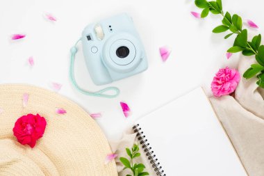 Düz yatıyordu moda ofis masası. Mavi nane modern film anlık kamera, hasır şapka, boş kağıt not defteri, pembe gül çiçek tomurcukları ve beyaz arka plan üzerinde yaprakları ile Kadın çalışma alanı. Üst görünüm kadınsı tablo.