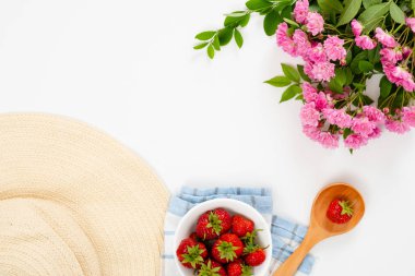 Çilek, hasır şapka, tahta kaşık, pembe gül çiçekleri ile yaz sabahı kahvaltı konsepti. Düz döşeme, üst görünüm, genel merkez.