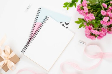 Zarif kağıt not defteri, pembe çiçekler boquet, gixf kutusu, beyaz arka plan üzerinde kurdele ile üst görünüm kadınsı ev ofis masası. Minimal düz lay stil kompozisyon, güzellik blogger çalışma alanı kavramı.
