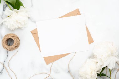 Beyaz şakayık çiçekler ve ip ile mermer arka plan üzerinde üst görünümü boş düğün davetiye kartı. Minimal flatlay tarzı kompozisyon, düğün ve evlilik kavramı. Güzellik veya moda günlüğü afiş mockup