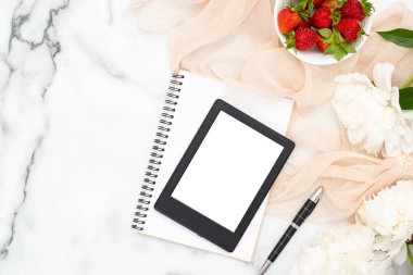 Üst görünüm e-kitap okuyucu, kağıt not defteri, şakayık çiçekler, çilek, mermer arka plan üzerinde pastel renkli eşarp. Kadınsı aksesuarları ile minimal düz yatıyordu stil kompozisyon. Moda veya güzellik blog afiş.