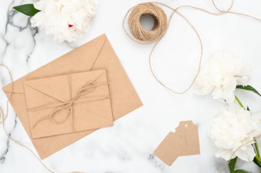 Mermer arka plan üzerinde üst görünüm düğün kadınsı aksesuarlar. Zanaat kağıt zarf, ip, etiketler ve beyaz şakayık çiçekleri ile Minimal düz yatıyordu tarzı kompozisyon. Düğün ve evlilik konsepti.