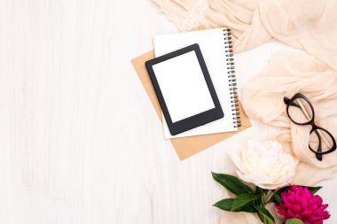 Kadın öğeleri ile Moda blogger ev ofis masası: modern e-kitap okuyucu, kağıt not defteri, bej eşarp, şakayık çiçekler, gözlük. Üst görünüm, ihale minimal düz döşeme stil kompozisyonu.