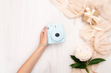 Kadın el şakayık çiçekleri ile ahşap bir arka plan üzerinde modern kamera tutan. Üst görünüm, ihale minimal düz döşeme tarzı kompozisyon. Kadın masası, moda blogger, güzellik ve teknoloji konsepti