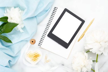 Üst görünüm e-kitap okuyucu, kağıt not defteri, şakayık çiçekler, mermer arka plan üzerinde pastel renk eşarp. Kadınsı altın aksesuarlar ile minimal düz yatıyordu stil kompozisyon. Moda veya güzellik günlüğü afiş mockup