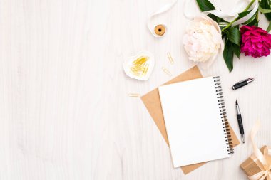 Düz yatıyordu ev ofis masası. Kağıt defter, pion çiçek buketi, ahşap arka plan üzerinde altın aksesuarlar ile Kadın çalışma alanı. Üst görünüm kadınsı arka plan. Moda günlüğü afiş şablonu.