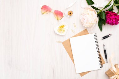 Düz yatıyordu ev ofis masası. Kağıt defter, pion çiçek buketi, altın aksesuarlar, ahşap arka plan üzerinde güneş gözlüğü ile Kadın çalışma alanı. Üst görünüm kadınsı arka plan. Moda blog afiş mockup.