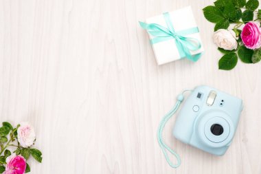 Modern polaroid kamera, hediye kutusu, kadınsı aksesuarlar, ahşap arka plan üzerinde güller. Üst görünüm, ihale minimal düz döşeme tarzı kompozisyon. Kadın masası, moda blogger, güzellik teknolojisi kavramı