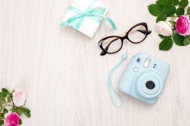 Modern polaroid kamera, hediye kutusu, gözlük, kadınsı aksesuarlar, ahşap arka plan üzerinde gül. Üst görünüm, ihale minimal düz döşeme tarzı kompozisyon. Kadın masası, moda blogger, güzellik teknolojisi