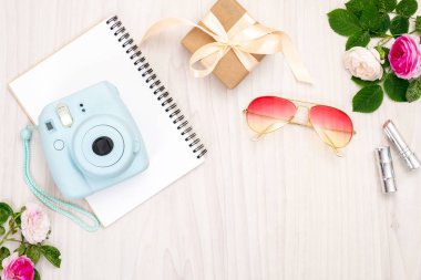 Modern polaroid kamera, hediye kutusu, güneş gözlüğü, kadınsı aksesuarlar, ahşap arka plan üzerinde gül. Üst görünüm, ihale minimal düz döşeme tarzı kompozisyon. Kadın masası, moda blogger, güzellik teknolojisi