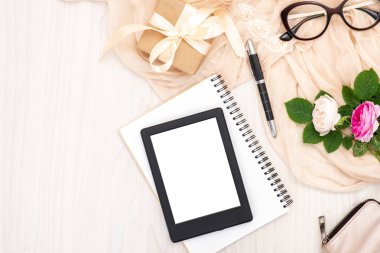 Düz yatıyordu e-kitap okuyucu, kağıt not defteri, gözlük, gül çiçekler, hediye kutusu, ahşap masada bej eşarp. Üst görünüm kadın ev ofis çalışma alanı, kadınsı arka plan. Moda günlüğü, güzellik ve teknoloji.