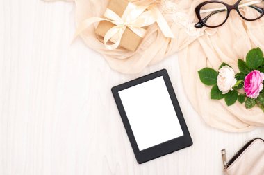 Düz yatıyordu e-kitap okuyucu, gözlük, gül çiçekleri, hediye kutusu, ahşap masa üzerinde bej eşarp. Üst görünüm kadın ev ofis çalışma alanı, kadınsı arka plan. Moda blog afiş, güzellik ve teknoloji kavramı.