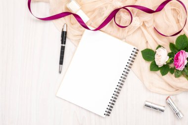 Düz kağıt defter, gül çiçekler, kurdele, bej eşarp, ahşap masada ruj yatıyordu. Üst görünüm kadın ev ofis çalışma alanı, kadınsı arka plan. Moda blog afiş, güzellik ve teknoloji kavramı.