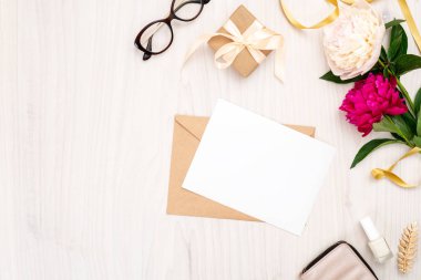 Düz yatıyordu ev ofis masası. Boş kağıt kartı, zanaat zarf, şakayık çiçek buketi, ahşap arka plan üzerinde altın aksesuarlar ile Kadın çalışma alanı. Üst görünüm kadınsı arka plan. Moda blog afiş