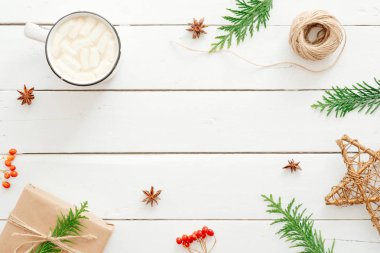 Noel kompozisyonu. Çerçeve köknar ağacı dalları, dekorasyon, marshmallow ile sıcak çikolata fincan, ahşap beyaz arka plan üzerinde kırmızı berry yapılmış. Düz yatıyordu, üstten bak. Yeni yıl, kış, Noel konsepti