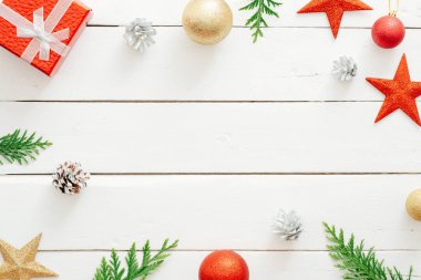 Noel minimal kompozisyon. Çerçeve Noel süslemeleri, kırmızı yıldız, hediye kutusu, topları, konileri, ahşap beyaz arka plan üzerinde köknar ağacı dalları yapılmış. Yeni yıl, Noel konsepti. Düz döşeme, üst görünüm