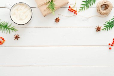 Noel kompozisyonu. Çerçeve köknar ağacı dalları, hediye kutuları, marshmallow ile sıcak çikolata fincan, ahşap beyaz arka plan üzerinde kırmızı berry yapılmış. Düz yatıyordu, üstten bak. Yeni yıl, kış, Noel konsepti
