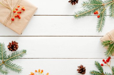 Noel kompozisyonu. Hediye kutusu, köknar ağacı dalları, koniler, ahşap beyaz arka plan üzerinde kırmızı berry yapılmış Noel çerçevesi. Düz döşeme, üst görünüm, kopyalama alanı. Noel arka plan, Xmas kartpostal şablonu