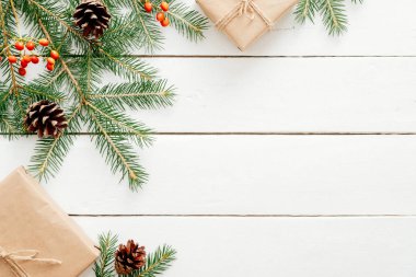 Noel kompozisyonu. Noel çerçeve köknar ağacı dalları, kırmızı berry, hediye kutuları, ahşap beyaz arka plan üzerinde koniler yapılmış. Düz döşeme, üst görünüm, kopyalama alanı. Noel, Yeni Yıl, kış tatili konsepti