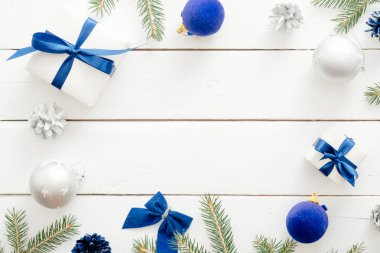 Noel kompozisyonu. Çerçeve köknar ağacı dalları, mavi süslemeler, hediye kutuları, koniler, beyaz ahşap arka plan üzerinde topları yapılmış. Düz döşeme, üst görünüm, kopyalama alanı. Yeni yıl, Noel, kış konsepti.