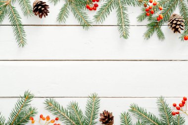 Noel çerçeve köknar ağacı dalları, kırmızı çilek, rustik ahşap beyaz arka plan üzerinde çam kozalağa yapılmış. Noel, Yeni Yıl, kış tatilleri kavramı. Düz döşeme, üst görünüm, kopyalama alanı