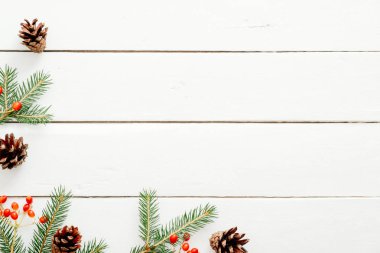 Noel çerçeve köknar ağacı dalları, kırmızı çilek, rustik ahşap beyaz masa üzerinde çam kozalağı yapılmış. Noel, Yeni Yıl, kış tatilleri kavramı. Düz döşeme, üst görünüm, kopyalama alanı