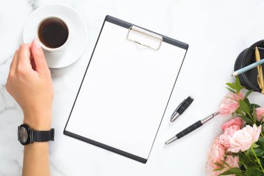 Boş karton, pembe gül çiçek buketi, kadın elinde kahve fincanı, beyaz mermer taş arka plan üzerinde kırtasiye ile modern ev ofis masası çalışma alanı. Flatlay, üst görünüm.