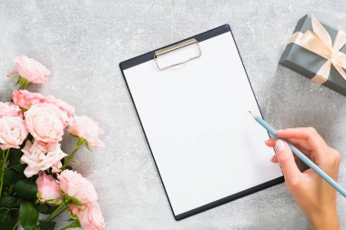 Gül çiçekleri ile Home ofis masası çalışma alanı, hediye kutusu, kadın el beton taş arka plan üzerinde karton bir mesaj yazmak. Düz yatıyordu, üst görünüm modern moda blog şablonu.