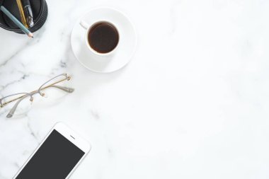 Kahve fincanı, cep telefonu, gözlük, kırtasiye beyaz mermer taş arka plan üzerinde ayarlanmış modern ev ofis masası çalışma alanı. Flatlay, üst görünüm, kopyalama alanı. Güzellik blogger işyeri konsepti.