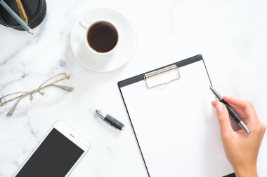 Kadın el kahve fincanı, kırtasiye ve beyaz mermer arka plan üzerinde aksesuarları ile modern ev ofis çalışma alanı üzerinde boş pano bir mesaj yazmak. Düz döşeme, üst görünüm.