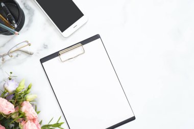 Boş kağıt pano mockup ile Modern ev ofis masası çalışma alanı, gül çiçekler, gözlük, akıllı telefon, beyaz mermer arka plan üzerinde kırtasiye. Flatlay, üst görünüm.