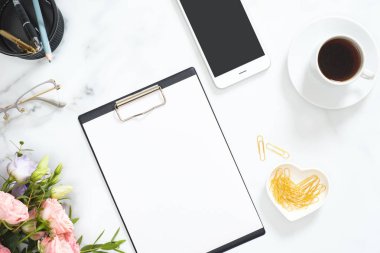 Boş kağıt pano mockup, kahve fincanı, akıllı telefon, gül çiçek buketi, gözlük, beyaz mermer arka plan üzerinde altın kırtasiye ile Modern ev ofis masası çalışma alanı. Flatlay, üst görünüm.
