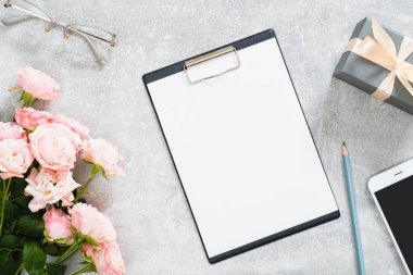 Kağıt pano mockup ile Modern ev ofis çalışma alanı, gül çiçekleri, hediye kutusu, gözlük, beton taş arka plan üzerinde cep telefonu. Düz döşeme, üst görünüm.