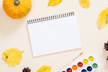 Sonbahar kompozisyonu. Kağıt not defteri veya albüm, turuncu kabak, kuru sonbahar yaprakları, pastel bej arka plan üzerinde ayarlanmış suluboya boyama. Düz yatıyordu, üstten bak, tepede. Sonbahar, eğitim, çizim konsepti