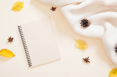 Sonbahar kompozisyonu. Kağıt not defteri, kuru sonbahar yaprakları, örme eşarp, pastel bej arka plan üzerine koni. Düz döşeme, üst görünüm, kopyalama alanı. Sonbahar minimal kavramı