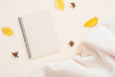 Sonbahar kompozisyon, Kağıt not defteri, örme eşarp, pastel bej arka plan üzerinde kuru sonbahar yaprakları. Sonbahar moda konsepti, minimal düz döşeme stil seti, üst görünüm.