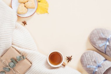Sonbahar flatlay kompozisyon. Beyaz örme ekose, hediye kutusu, terlik, çay bardağı, pastel bej arka plan üzerinde düşmüş yaprakları ile Kadınsı masaüstü. Düz yatıyordu, üstten bak. Sonbahar, sonbahar konsepti.