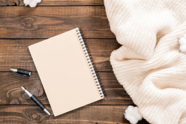 Flatlay sonbahar kompozisyon. Kadın moda beyaz kazak, boş sayfa, kalem, ahşap arka plan üzerinde pamuk ile kağıt not defteri. Düz yatıyordu, üstten bak, tepede. Rahat ev masası, hygge, sonbahar sonbahar konsepti