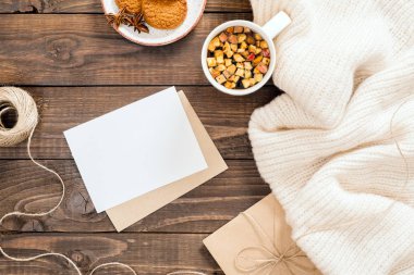 Beyaz yün ekose, boş kağıt kartı mockup, zarf, sıcak çay fincan, kurabiye, ip ile Sonbahar veya kış flatlay kompozisyon. Rahat ev masası, tatil hygge kavramı. Düz döşeme, üst görünüm, genel merkez.