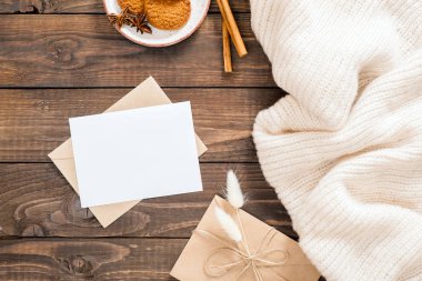 Beyaz yün ekose, boş kağıt kartı mockup, zarf, tarçın çubukları, çerezleri, kuru çiçekler ile Sonbahar veya kış flatlay kompozisyon. Rahat ev masası, hygge konsepti. Düz döşeme, üst görünüm, genel merkez.