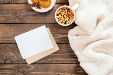Beyaz yün ekose, boş kağıt kartı mockup, zarf, sıcak çay fincan, çerezleri ile Sonbahar veya kış flatlay kompozisyon. Rahat ev masası, tatil hygge kavramı. Düz döşeme, üst görünüm, genel merkez.