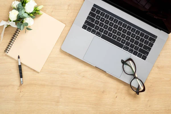 Mesa de escritorio moderna de madera con computadora portátil, bloc de notas de papel, bolígrafo, planta suculenta, ramo de flores de rosas. Composición de estilo laico plano mínimo con espacio de copia, vista superior. Espacio de trabajo femenino . —  Fotos de Stock